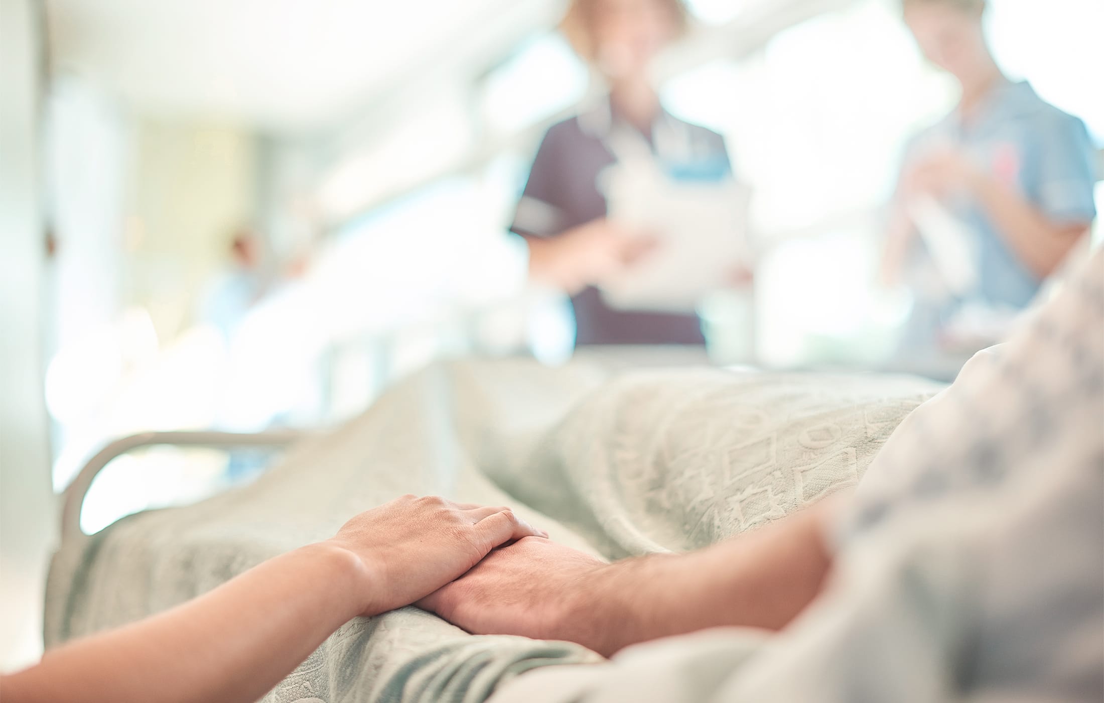 Close-up of a hospital patient in bed holding hands with a visitor